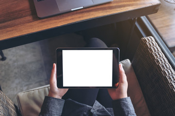 Mockup image of woman's hands holding black tablet pc with blank white screen on thigh with laptop in modern cafe