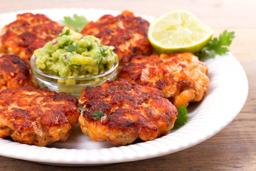 Salmon patties or cakes, lime and avocado on white plate. Fritters of fish. Salmon burgers. Healthy snack or take-away lunch bites