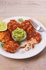 Salmon patties or cakes, lime and avocado on white plate. Fritters of fish. Salmon burgers. Healthy snack or take-away lunch bites
