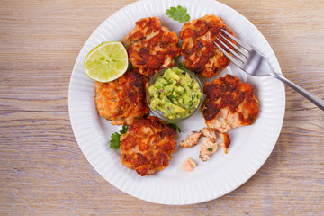 Salmon patties or cakes, lime and avocado on white plate. Fritters of fish. Salmon burgers. Healthy snack or take-away lunch bites, overhead