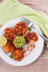 Salmon patties or cakes, lime and avocado on white plate. Fritters of fish. Salmon burgers. Healthy snack or take-away lunch bites, overhead