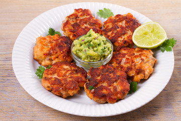 Salmon patties or cakes, lime and avocado on white plate. Fritters of fish. Salmon burgers. Healthy snack or take-away lunch bites