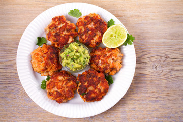 Salmon patties or cakes, lime and avocado on white plate. Fritters of fish. Salmon burgers. Healthy snack or take-away lunch bites, overhead