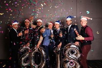 Joyful group of cheerful friends celebrating the new year throwing confetti, holding the silver...