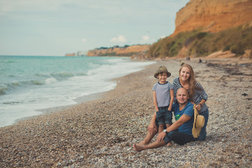Fototapeta na wymiar Lovely amazing scene of happy family of handsome father beautiful lady mother and cute little son boy posing together of sea side ocean stone beach on vacation relax wearing stylish clothes