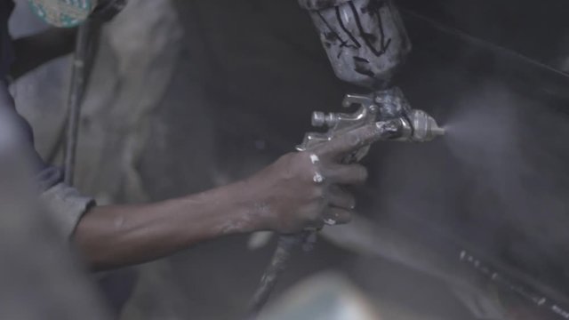 African mechanic spray paints car, slo-mo.