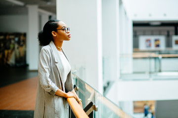 Serious african business student woman standing at railing in business center or shopping mall....