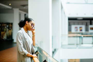 Serious african business student woman standing at railing in business center or shopping mall. Side view. Lifestyle, leisure and people concept.