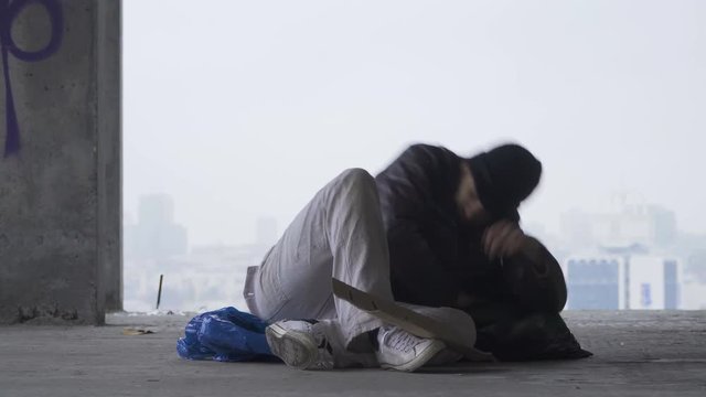 Homeless man goes to sleep on the garbage bag, urban background