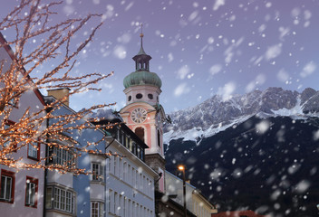 Roofs of Innsbruck with mountains on a background and Christmas lights on a foreground at winter snowy evening