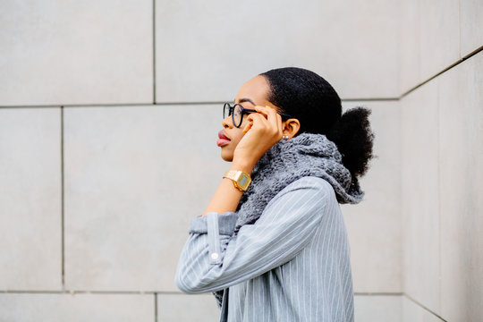 Side view of portrait beautiful african american business woman in glasses and gray kniitted snud over beige wall. Lifestyle, leisure and people concept.