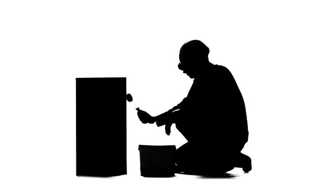Worker in a helmet paints a building with a roller. Silhouette. White background