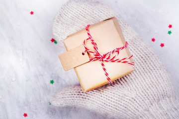 Women is holding a small gift box in hands worn in white knitted mittens