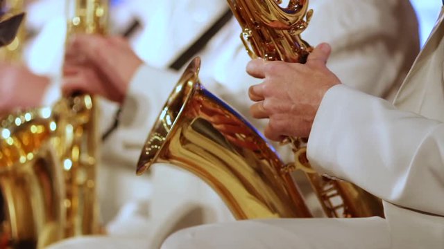 A man's hand in a white suit on a gold saxophone in a jazz band. Close-up. Shallow depth of field.