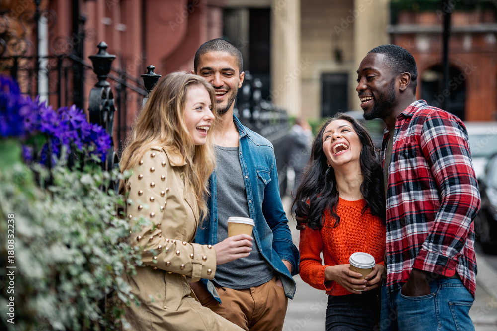 Wall mural Multiracial group of friends having fun together in London. Two girls and two boys, talking and laughing. Residential district with houses and cars on background. Lifestyle and friendship concepts.