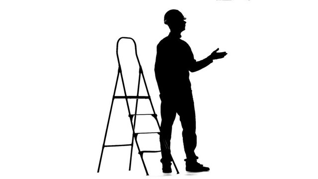 Engineer in a helmet stands near the stepladder. Silhouette. White background. Slow motion