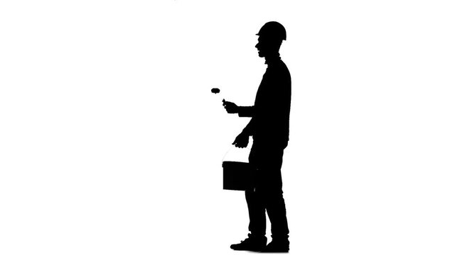 Worker in a helmet paints a building with a roller. Silhouette. White background. Slow motion