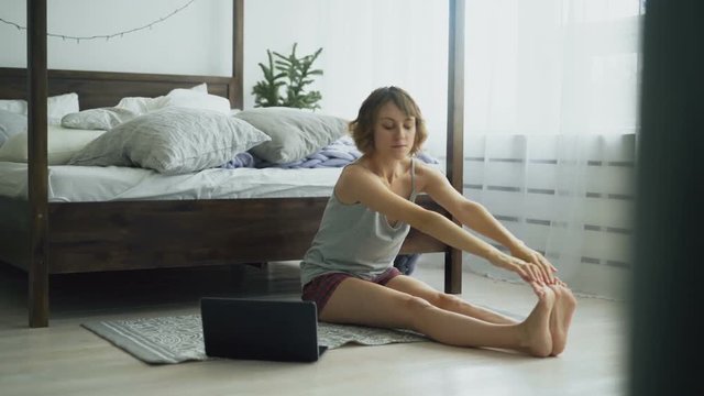 Young woman doing yoga with video tutorial on laptop