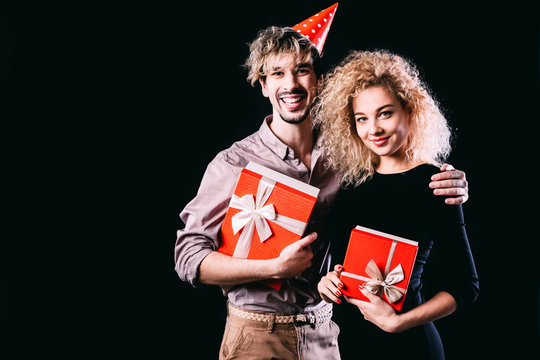 Happy couple hold red presents box, man and woman smile looking at camera embracing.