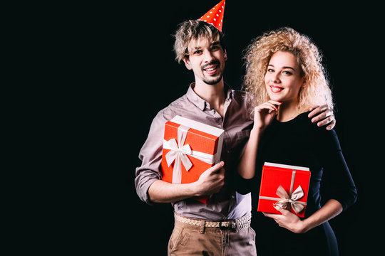 Happy couple with red gift boxes, man and woman smile looking at camera embracing, isolated on black.