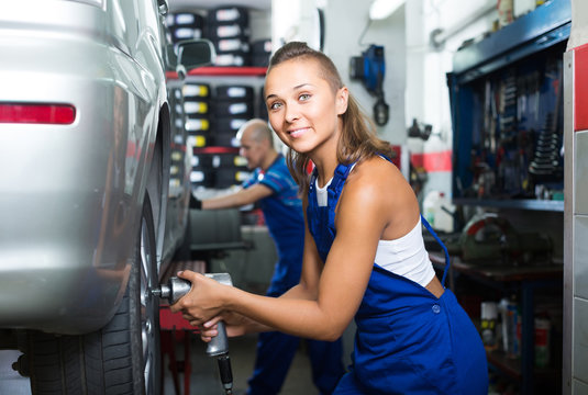woman technician fitting new tires to car at workshop