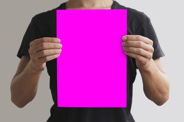 Man in black t shirt holding blank pink A4 paper vertically. Leaflet presentation. Pamphlet hold hands. Man show clear offset paper. Sheet template. Isolated on grey background