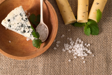 white cheese with mold in a wooden plate and yellow cheese on the flax napkin with salt crystals