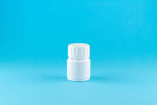Close up white pill bottle on blue background with copy space. Focus on foreground, soft bokeh. Pharmacy drugstore concept