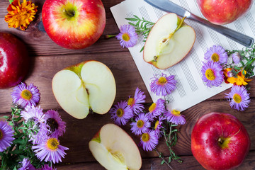 Red apples and slices of purple and yellow flowers, knife and notes on a wooden background, the atmosphere of the morning autumn day and melodies