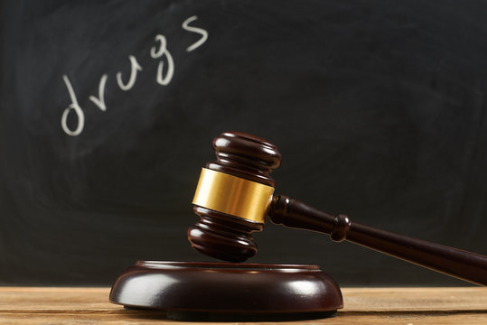 Judge gavel on wooden table at blackboard background writing the word "drugs".