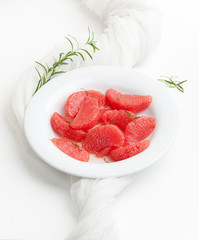 Peeled grapefruit slices and rosemary sprigs in a white plate on a white background.