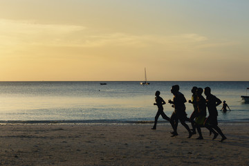 Group of people runs along ocean coast at sunset