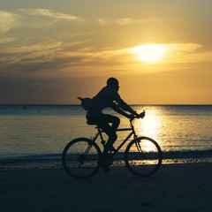 Fototapeta premium Man riding bicycle at sunset along the ocean coast