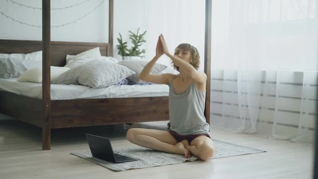 Young attractive woman doing yoga exercise and watching tutorial lesson on laptop computer at home