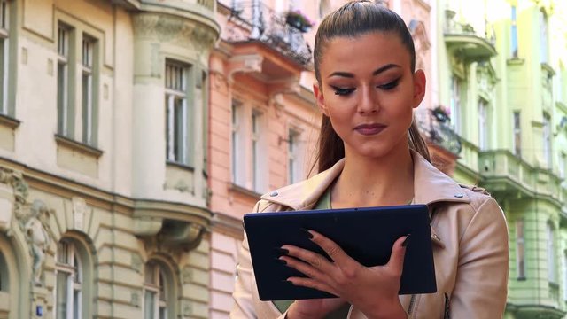 Young beautiful woman works on tablet in the city - buildings in the background