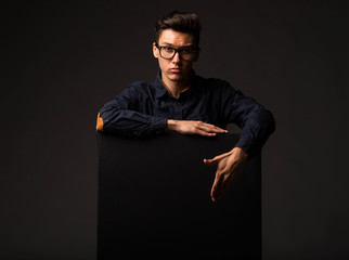 Young serious man portrait of a confident businessman showing presentation, pointing paper placard black background. Ideal for banners, registration forms, presentation, landings, presenting concept.