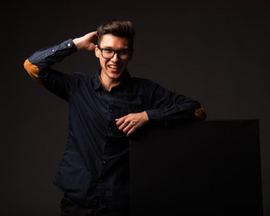 Young glad man portrait of a confident businessman showing presentation, pointing paper placard black background. Ideal for banners, registration forms, presentation, landings, presenting concept.