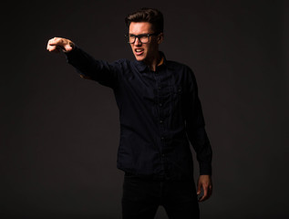Young angry man portrait of a confident businessman showing by hands on a black background. Ideal for banners, registration forms, presentation, landings, presenting concept.