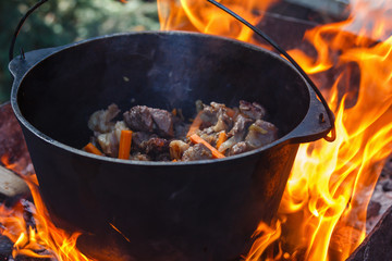 Tourist bowler with food on bonfire, cooking in the hike, outdoor activities. Preparation of pilaf.