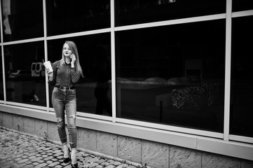 Fototapeta na wymiar Portrait of a beautiful woman in red blouse and casual jeans talking on mobile phone and holding a cup of coffee outside the huge shopping mall. Black and white photo.