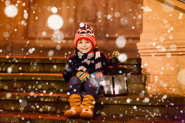 Little cute kid boy with with a light lantern on stairs near church.