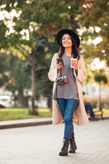 Modern asian woman holding mobile phone and coffee cup while walking in park outdoor