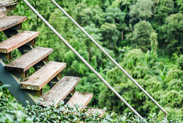 Rustic wooden stairs with steel pipe railing of a rural house Thailand. Green and fresh mountain landscape in background makes climbing up very joyful.