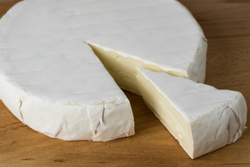 Round of Camembert cheese brie with triangle cut out on wood.