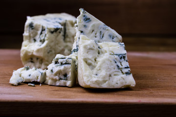 Danish blue or roquefort cheese macro shot on the cutting board with coarse edges and moldy veins exposed.