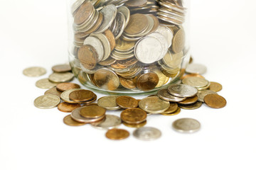 Close up coins in glass jar on white table. Coins scattered around. Isolated on white background.