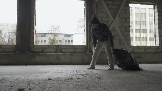 Dirty homeless drags a garbage bag in abandoned building