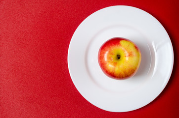 red-yellow apple on a white plate against the red background