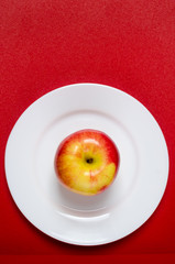 red-yellow apple on a white plate against the red background. vertical picture
