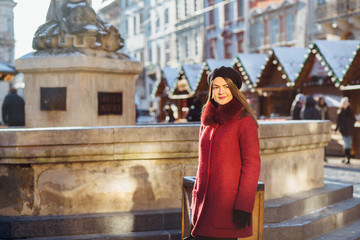 Stylish fashion girl of tourist in in red coat and black beret, posing in front of Christmas Fair in old town.